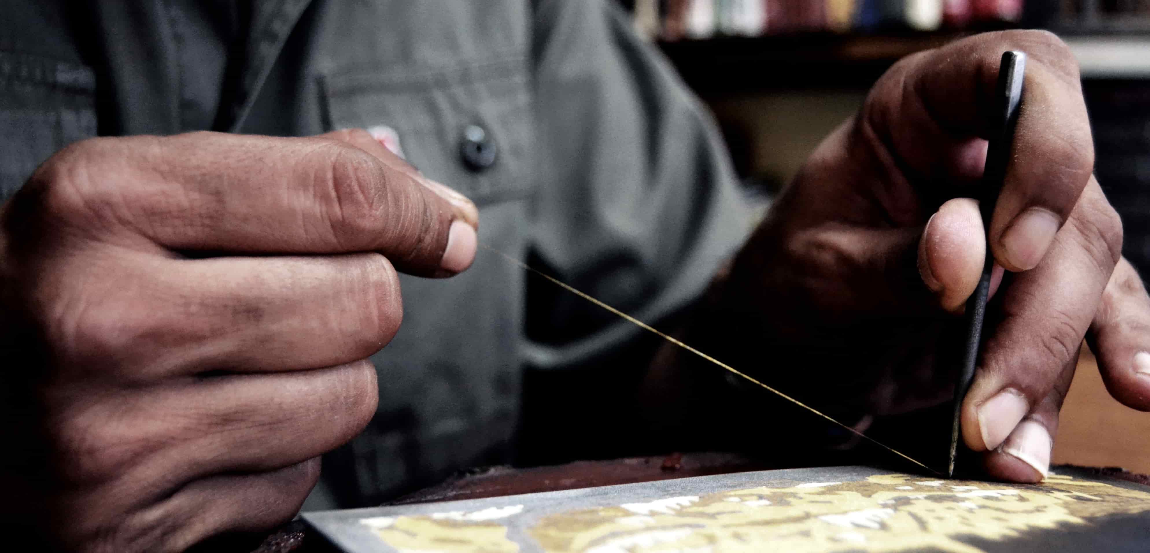 Primer plano de las manos del maestro artesano damasquinando con hilo de oro